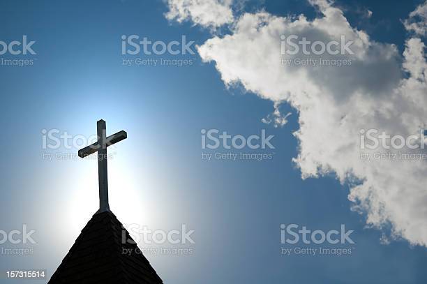 A wood cross on an old church steeple backlighted by a rising sun. Some copy space.